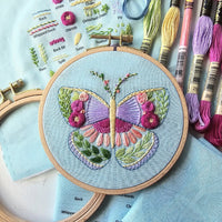 Embroidery hoop with a butterfly design surrounded by embroidery threads and tools.
