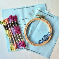Embroidery hoop with colorful threads and a pattern guide on a light surface.