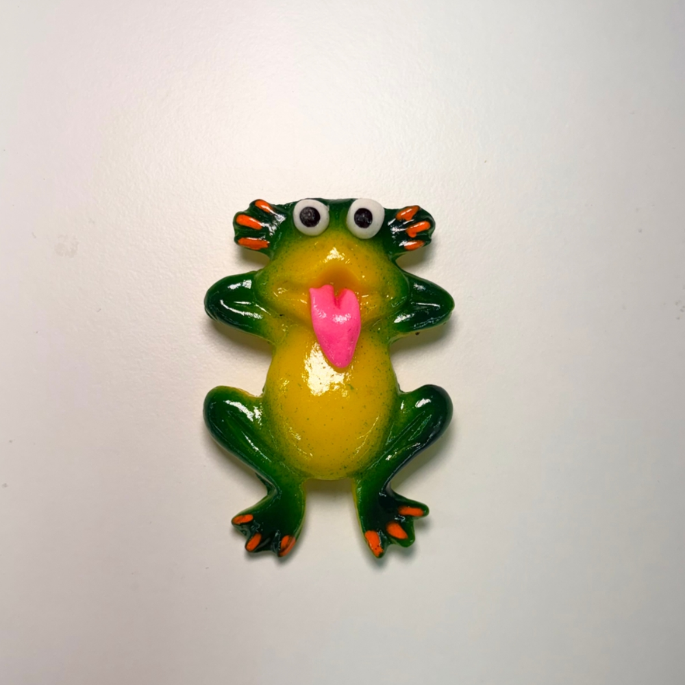 Clay magnet of a frog with its hands behind its head sticking its pink tongue out