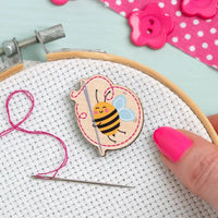 Embroidery hoop with a bee design and pink thread on a light blue background.
