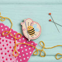 Bee-themed sewing tool with yellow thread on a light blue background