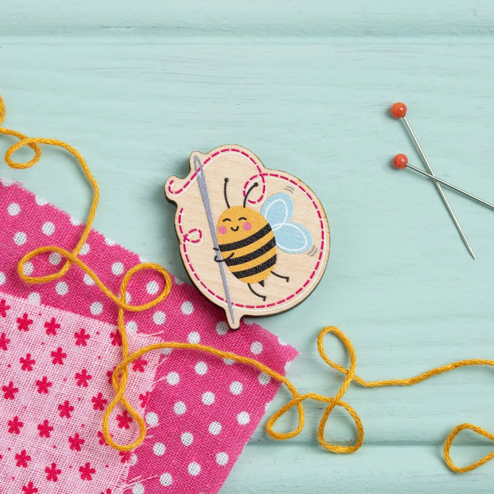 Bee-themed sewing tool with yellow thread on a light blue background