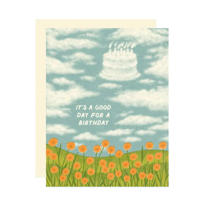 Birthday card with a field of orange flowers and a cloud shaped like a birthday cake reading “It’s a Good Day for a Birthday" on a white background.