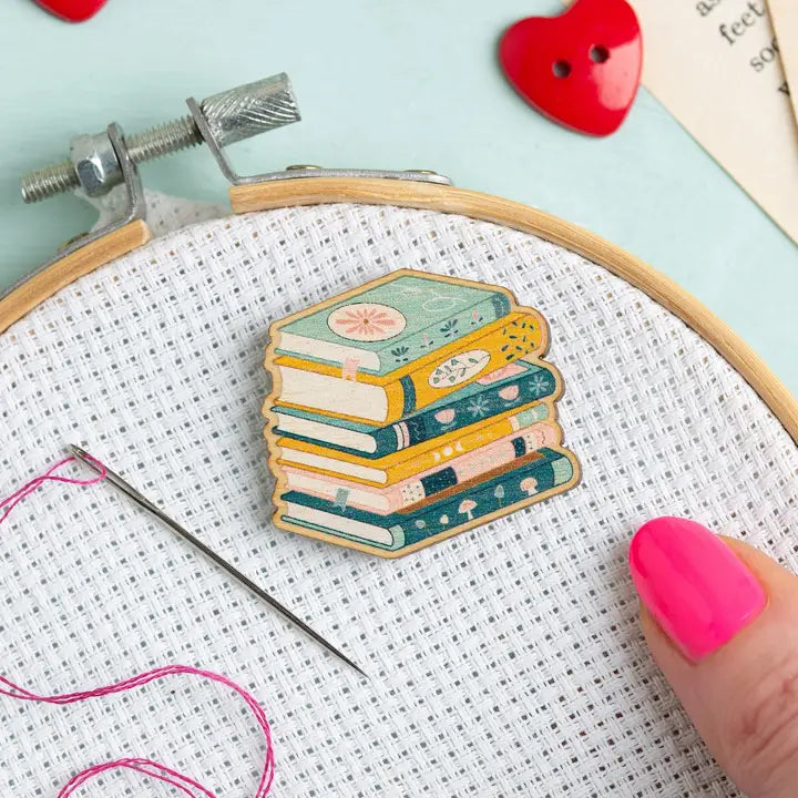 Wooden needle minder shaped like a stack of books on white aida fabric in an embroidery hoop