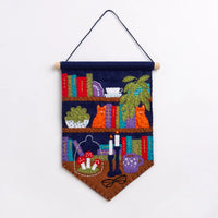 Colorful felt pennant featuring bookshelves, cats, plants, candles, mushrooms, glasses, and a coffee mug on a white background.