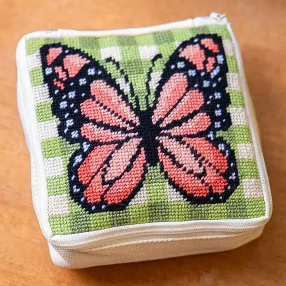 A square zipper pouch featuring a needlepoint design with a monarch butterfly on a green gingham background