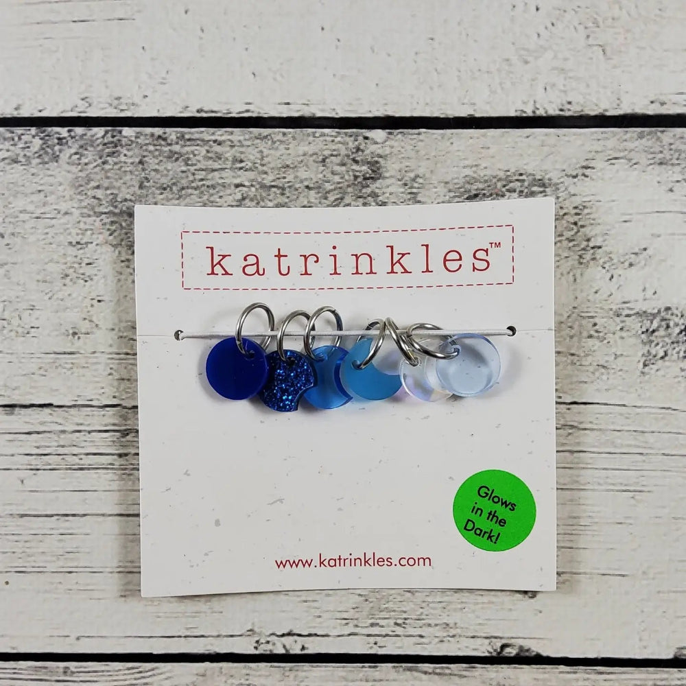 Set of blue and silver moon stitch markers on a 'katrinkles' branded card with a wooden background.