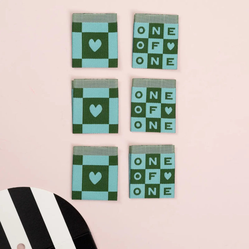 Six square labels with green and blue patterns and text on a pink background