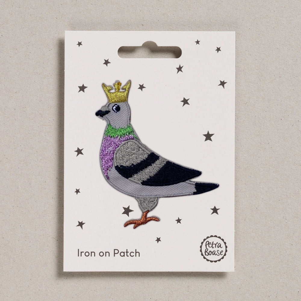 Embroidered patch of a pigeon with a crown on a white card with star patterns, branded 'Petra Boase'.
