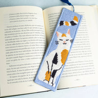 Needlepoint bookmark with a calico cat design on an open book with a light blue background