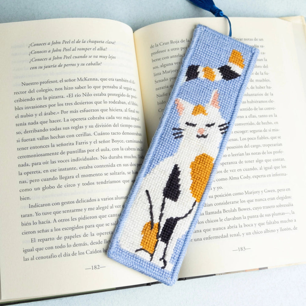 Needlepoint bookmark with a calico cat design on an open book with a light blue background