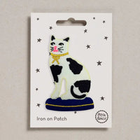 Black and white cat with gold bow iron on patch on a white card with 'Petra Boase' branding.