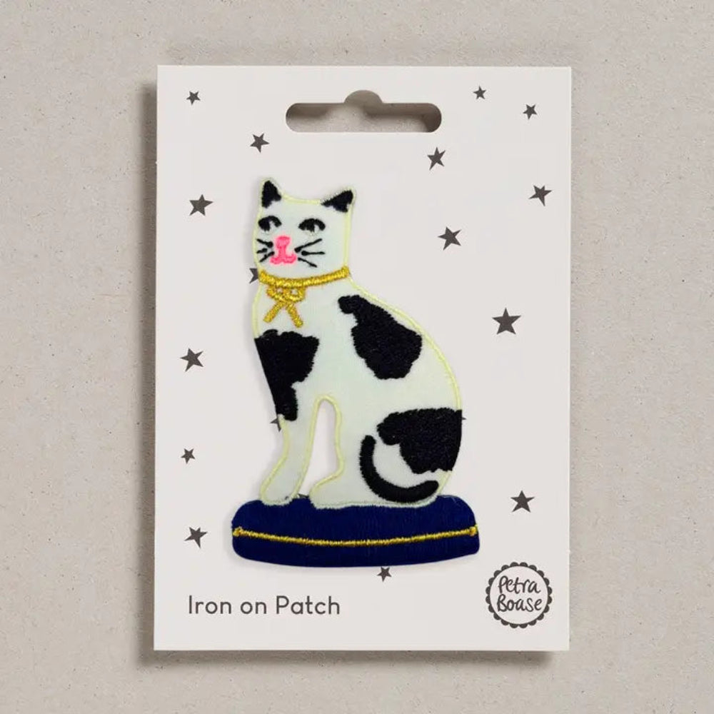 Black and white cat with gold bow iron on patch on a white card with 'Petra Boase' branding.