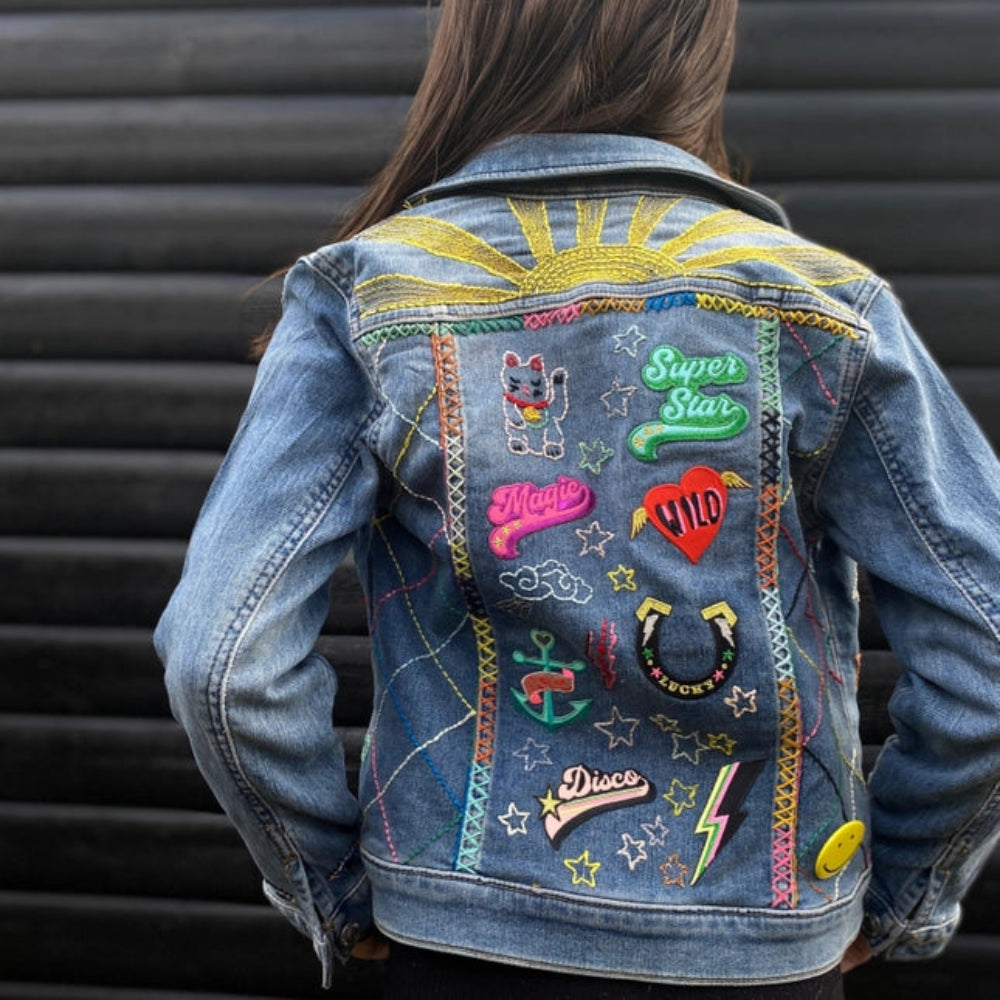 Denim jacket with colorful patches and embroidery on a person against a black background