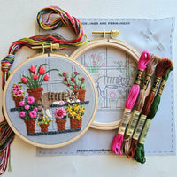 Embroidery hoop with floral and cat design, surrounded by colorful embroidery threads and a pattern sheet.