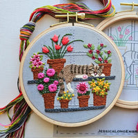 Embroidery hoop with a cat and flower design, colorful thread on the side.