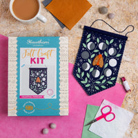 Felt craft kit with celestial design, scissors, and a cup of coffee on a textured surface.