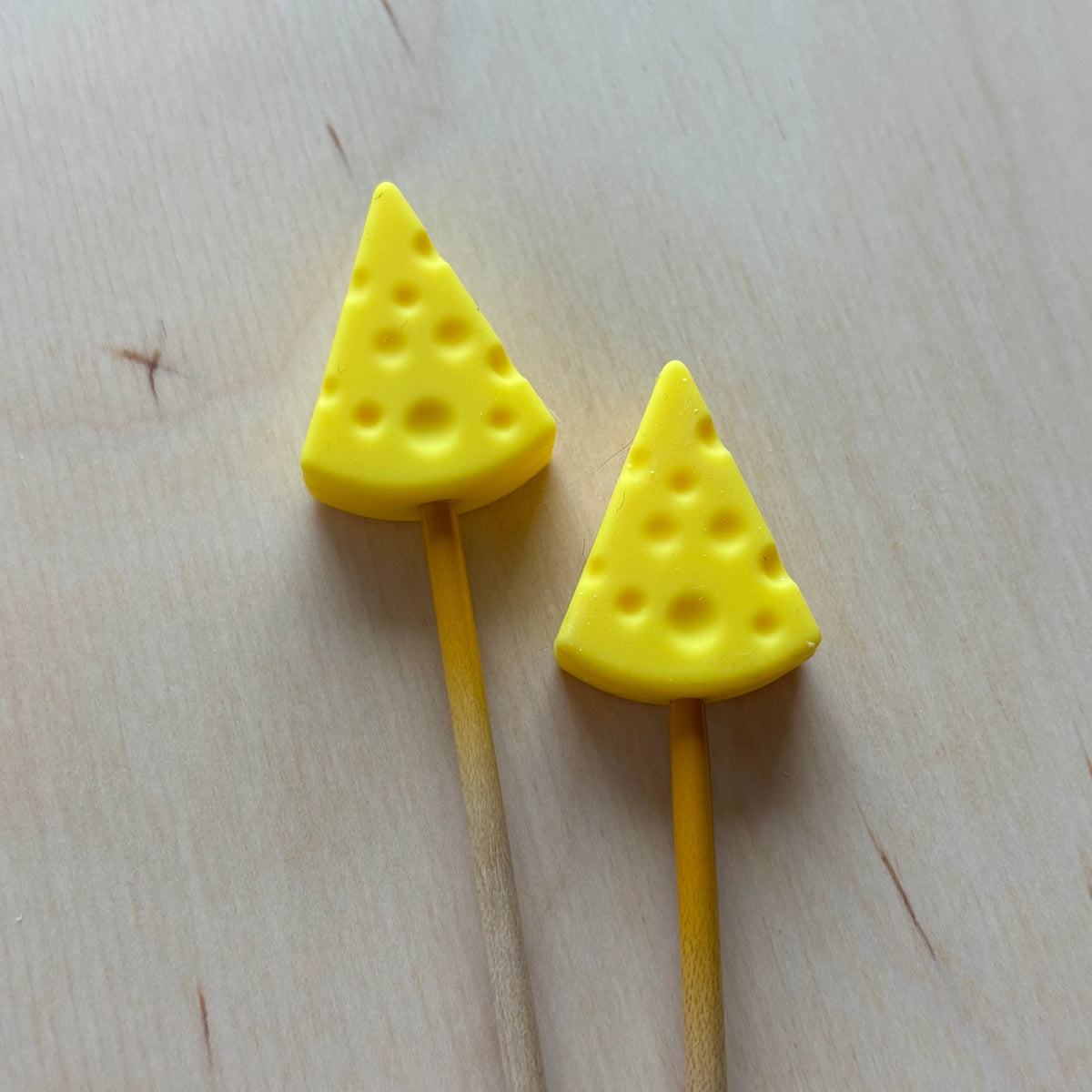 Two yellow cheese-shaped silicone ends on needles on a wooden surface.