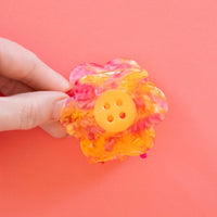 A hand is holding a pink and yellow  daisy with a yellow button center claw clip