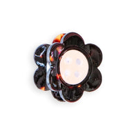 A mini daisy shaped claw clip with tortoise petals and a white button center is against a white background. 