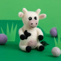 Felt cow sitting in a green background with purple balls
