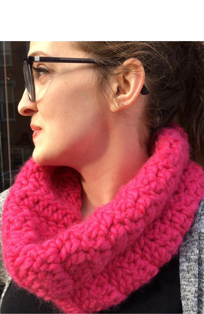 Woman in profile wearing a bright pink crocheted cowl.