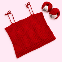 A red crochet tank top on a pink background, with two balls of cotton yarn.