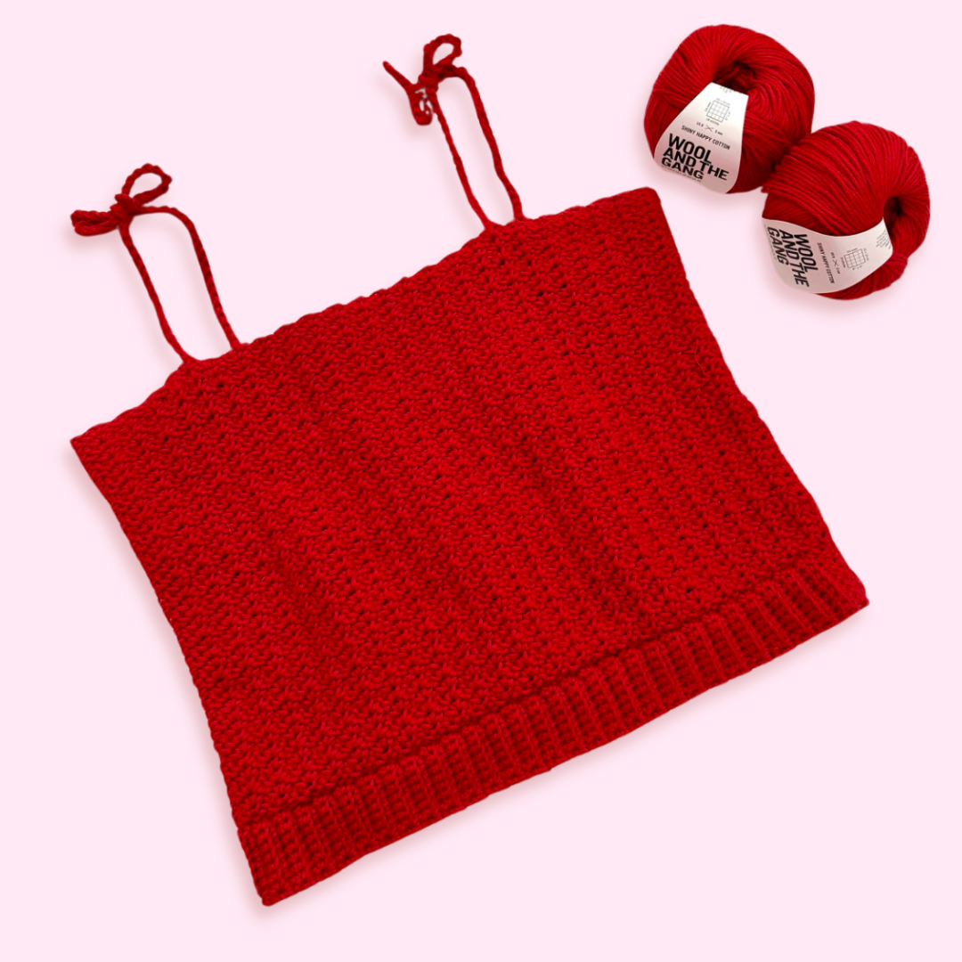 A red crochet tank top on a pink background, with two balls of cotton yarn.