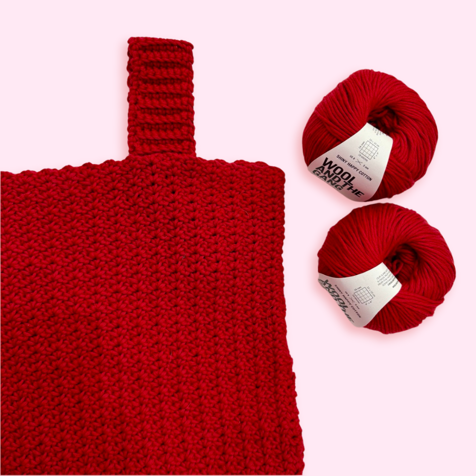 A close up of a red crochet tank top on a pink background, with two balls of cotton yarn.