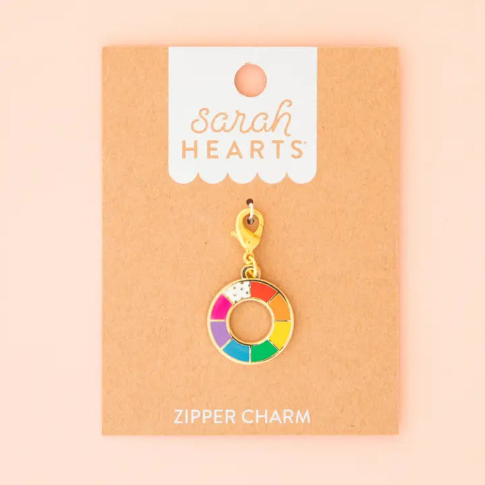 A zipper charm featuring a color wheel on Sarah Hearts packaging against a pink background.