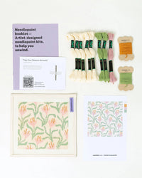Needlepoint kit with thread, patterns, and booklet on a white background