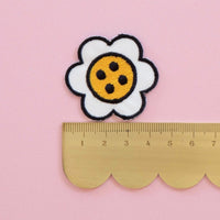 A scalloped ruler with a daisy button shaped patch on top
