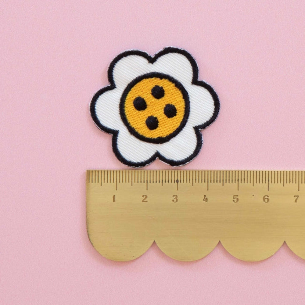 A scalloped ruler with a daisy button shaped patch on top