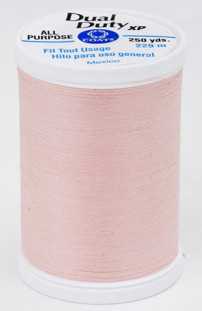 A spool of light coral pink Dual Duty XP sewing thread with a white label featuring blue and black text, set against a plain white background.
