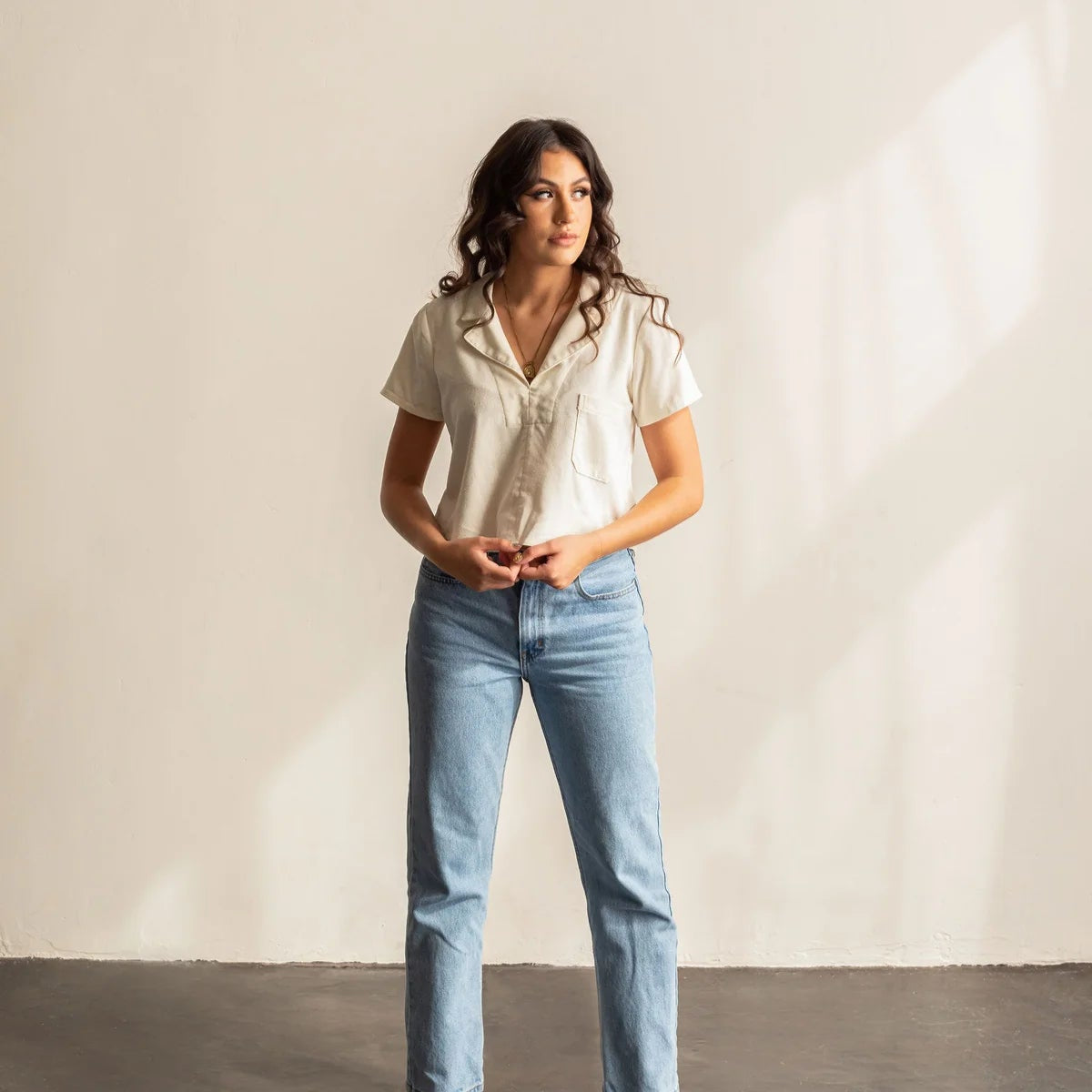 A woman wearing a white collard shirt and blue jeans.