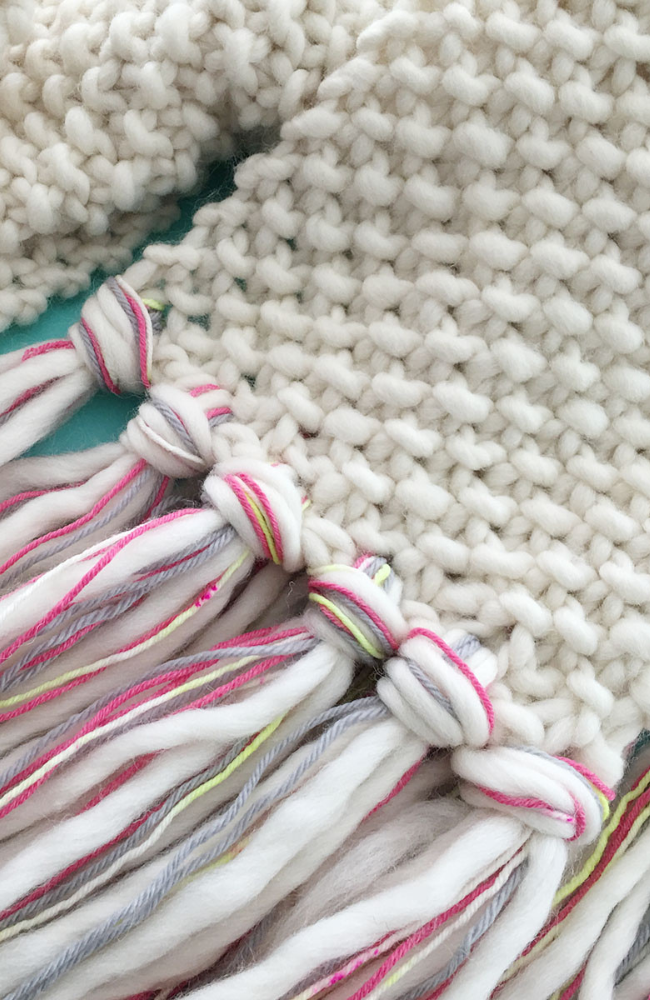 Cream knit scarf with gray, pink, yellow, and cream fringe.