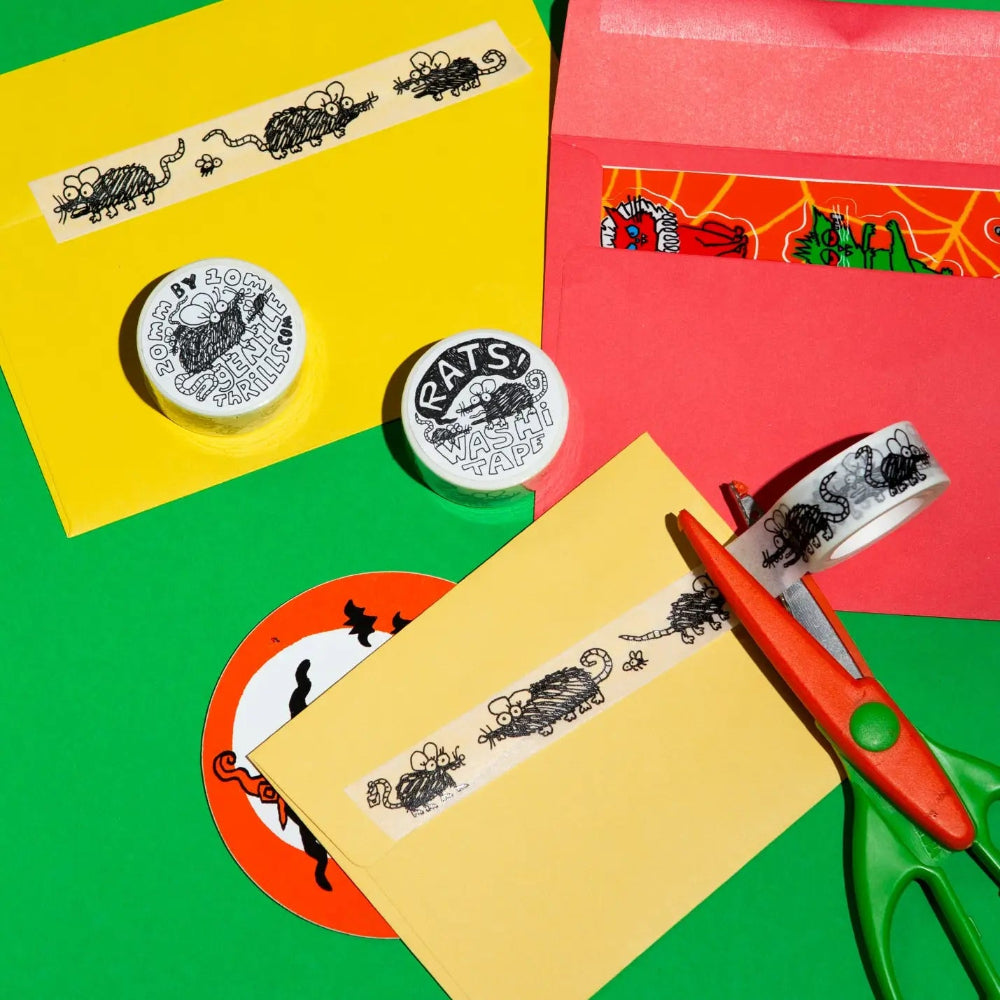 Colorful stationery items including rat themed washi tape, envelopes, and scissors on a multicolored background.