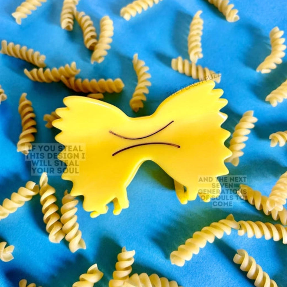 A bright yellow farfelle pasta clip surrounded by real farfelle pasta on a blue background. 