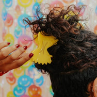 A person with curly hair wears a large bowtie pasta hair clip. 
