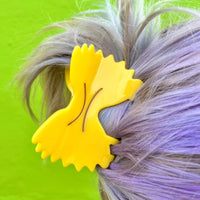 A bowtie pasta hair clip on purple hair against a green background. 