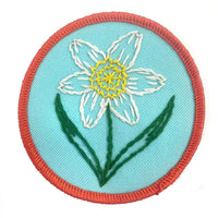 Embroidered patch with a white flower on a turquoise background with a red border