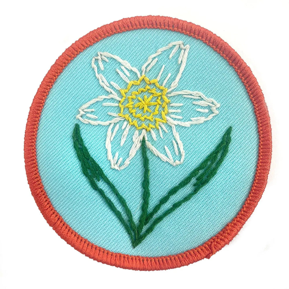 Embroidered patch with a white flower on a turquoise background with a red border