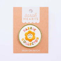 An iron-on patch featuring a smiling yellow flower with the words "Fabric Collector" in colorful letters on Sarah Hearts backing. 