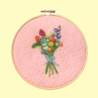 Embroidery hoop with a colorful bouquet of flowers on pink fabric against a yellow background