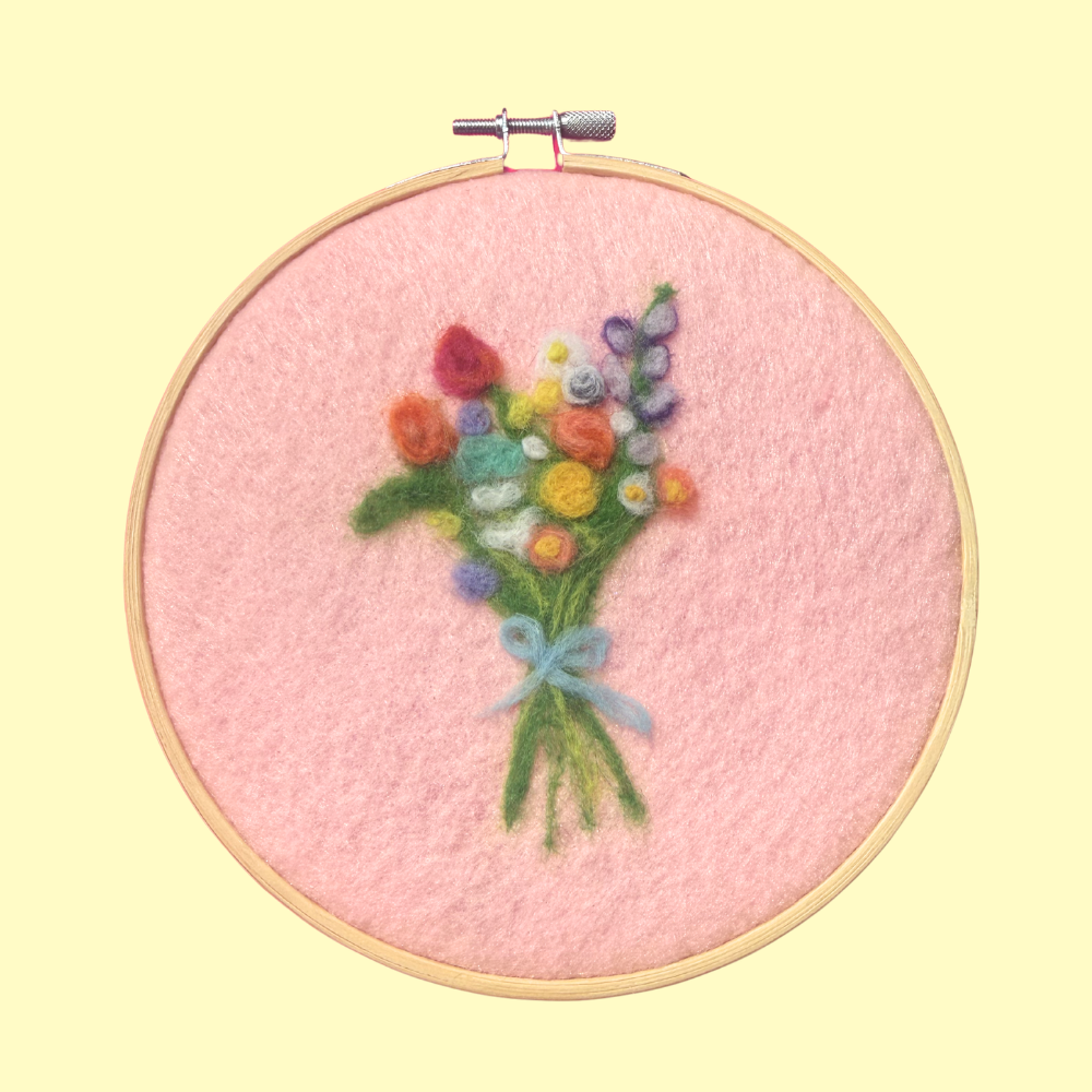 Embroidery hoop with a colorful bouquet of flowers on pink fabric against a yellow background