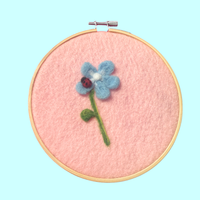 Embroidery hoop with a blue flower on pink fabric against a blue background