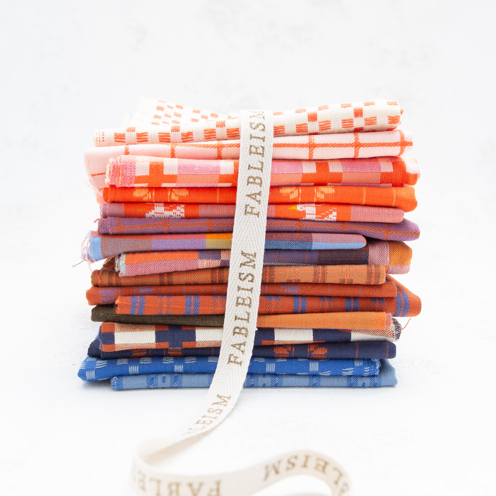 Stack of colorful fabric bundles tied with a ribbon on a white background