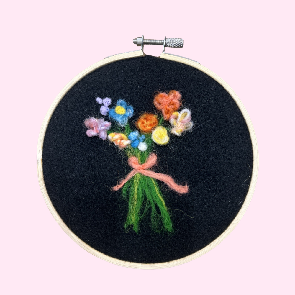 Embroidery hoop with a colorful bouquet of flowers on black fabric against a pink background