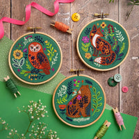 Embroidery hoops with animal designs(owl, fox, and bear) on a wooden surface with buttons and ribbons.