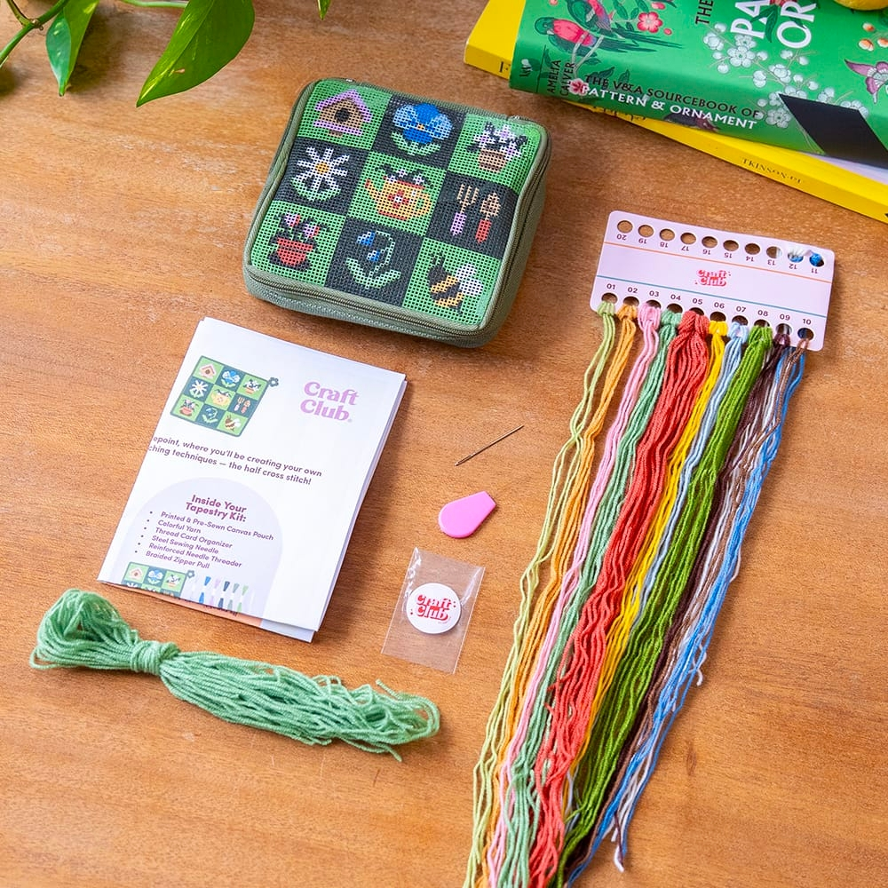 A kit for a square zipper pouch featuring a garden-themed needlepoint design, showing all the materials on a table